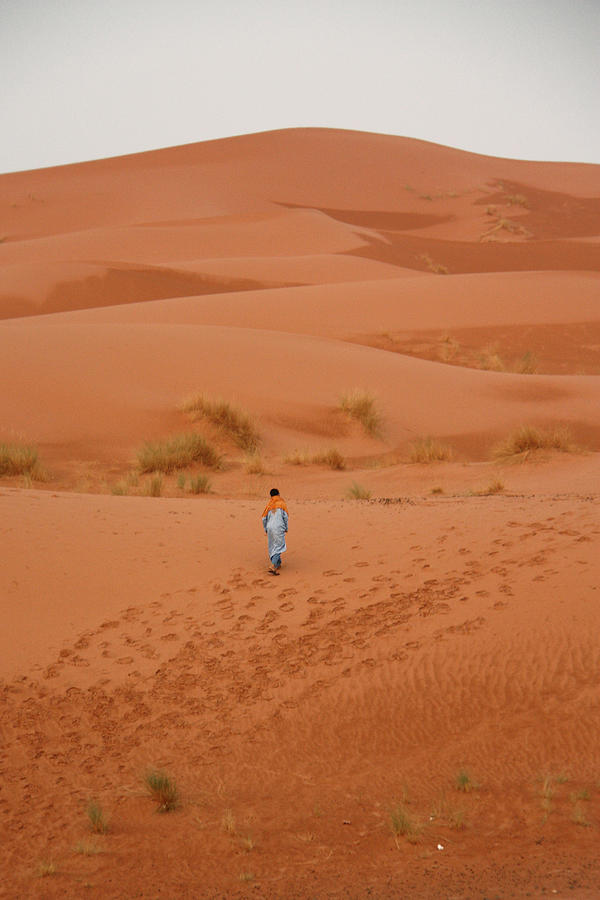 Young man walks alone in orange desert Photograph by David Oliete