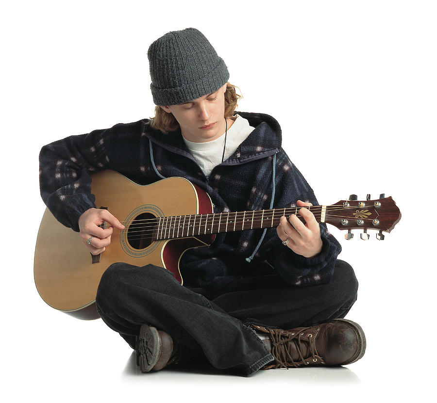 Young Man Wearing A Gray Hat Jacket And Dark Pants Sits On The Ground While Playing A Guitar Photograph by Photodisc