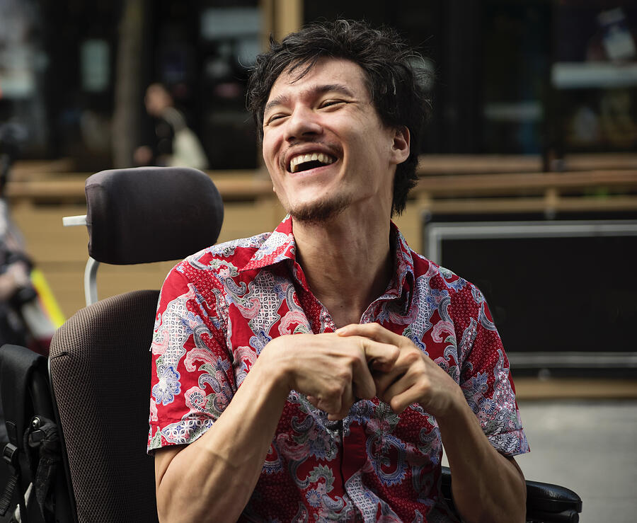 Young man with cerebral palsy laughing outdoors in city. Photograph by Martinedoucet Young man with cerebral palsy laughing outdoors in city. Photograph by Martinedoucet