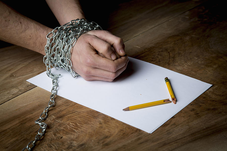 Young man with chains wrapped around his wrists, paper and broken pencil in front of him, focus on hands Photograph by Guido Cavallini