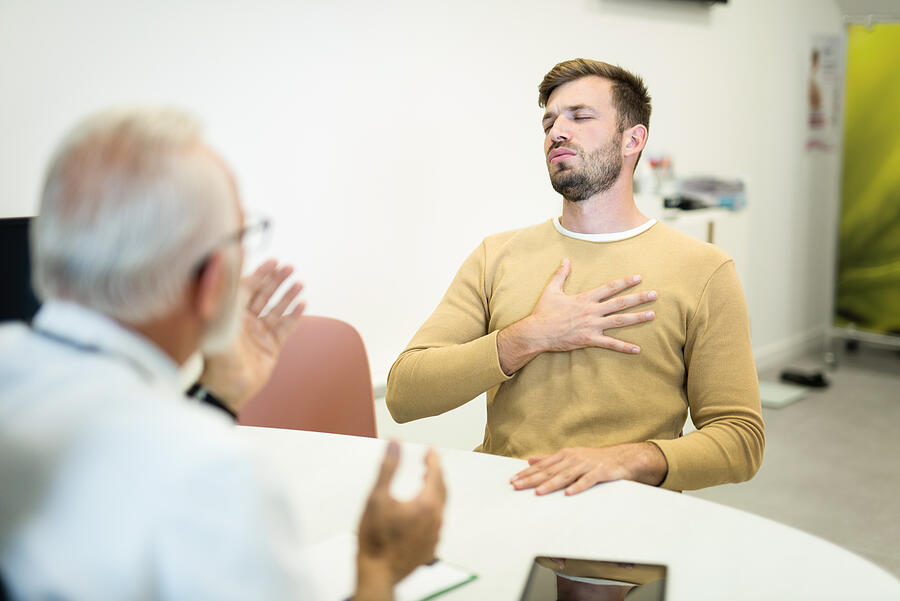 Young man with chest pain and breathing problems visiting a doctor. Photograph by DjelicS