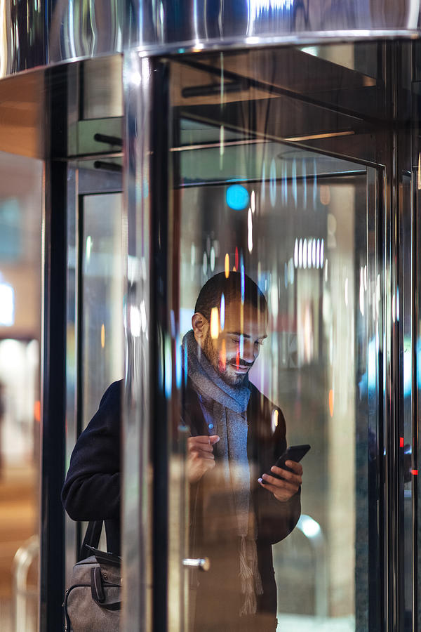 Young man with smart phone using revolving door Photograph by Shannon Fagan