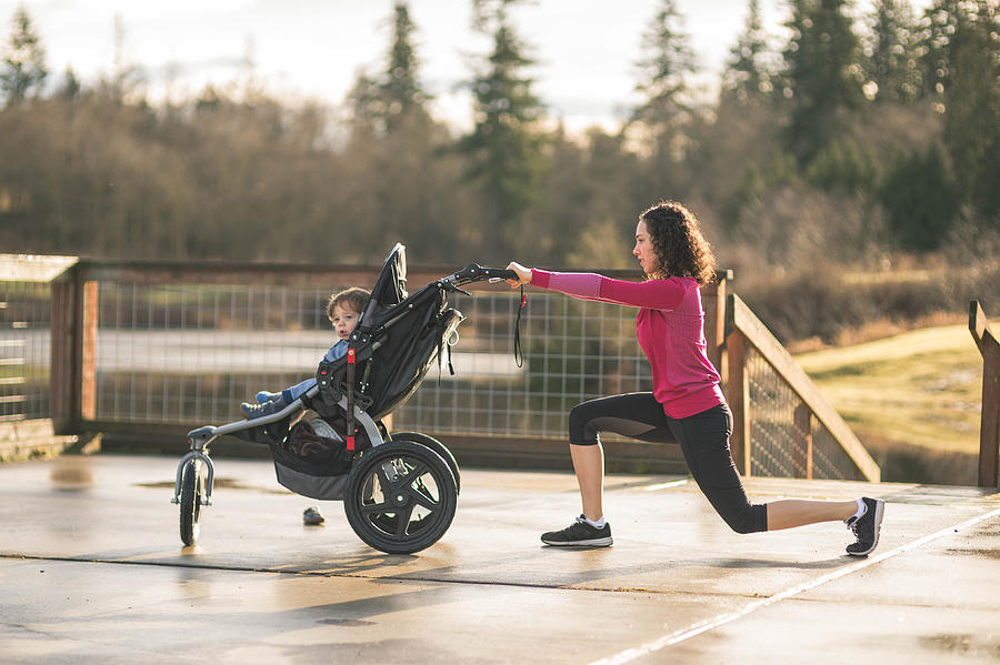 Young mom stretching next to child in baby stroller Photograph by FatCamera