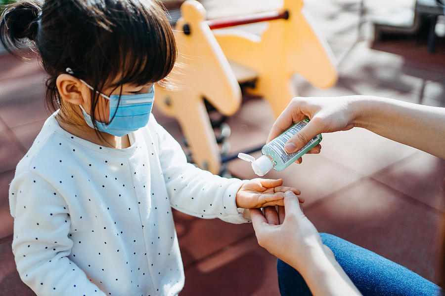 Young mother squeezing hand sanitizer onto little daughters hand in the playground to prevent the spread of viruses Photograph by D3sign