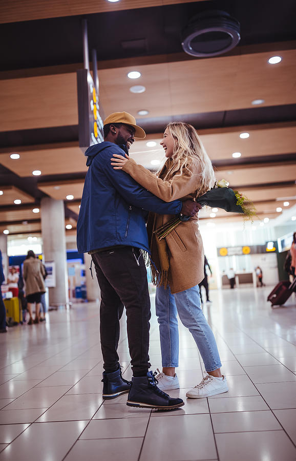 Young multi-ethnic friends meeting and embracing at airport Photograph by Wundervisuals