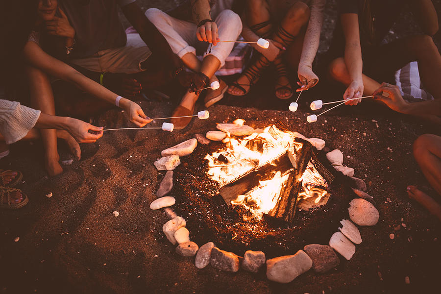 Young multi-ethnic friends roasting marshmallows over campfire at beach party Photograph by Wundervisuals