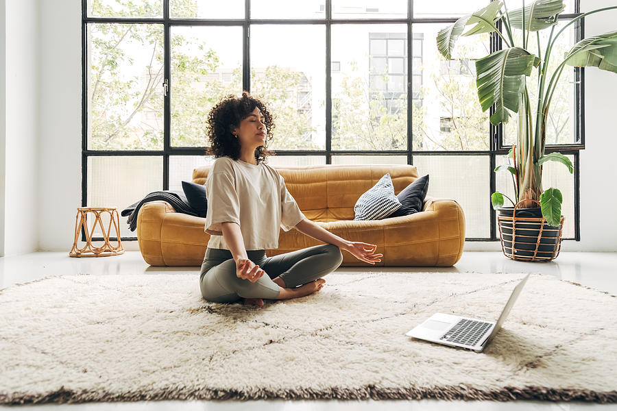 Young multiracial latina woman meditating at home with online video meditation lesson using laptop. Photograph by Daniel de la Hoz
