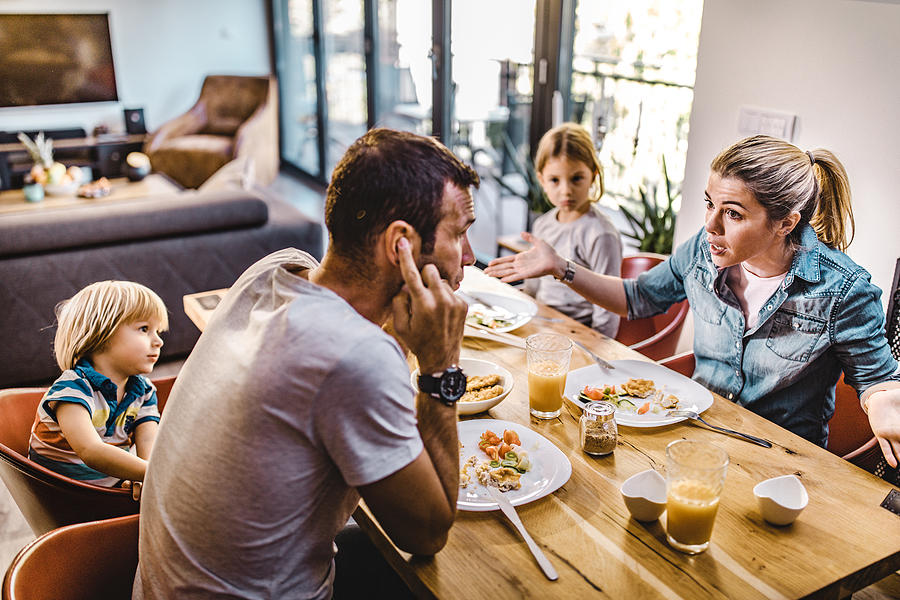 Young parents arguing while having lunch with their kids at home. Photograph by Skynesher
