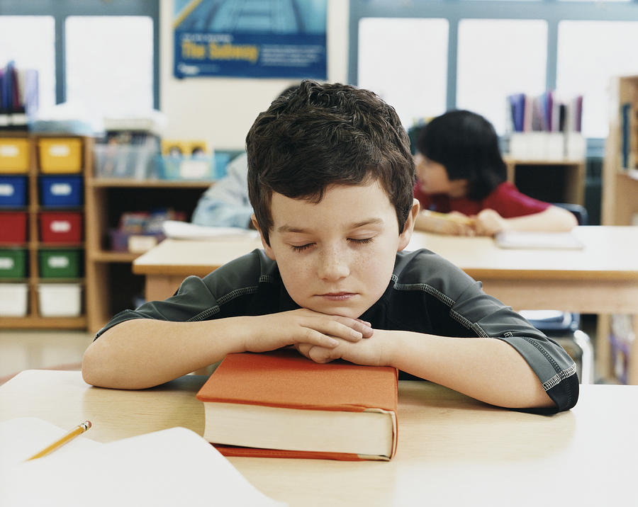 Young Primary Schoolboy Asleep at His Desk in the Classroom Photograph by Digital Vision.