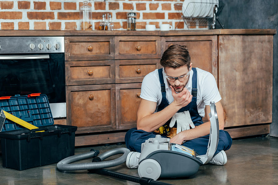 Young Repairman In Protective Glasses Looking At Broken Vacuum Cleaner Photograph by LightFieldStudios