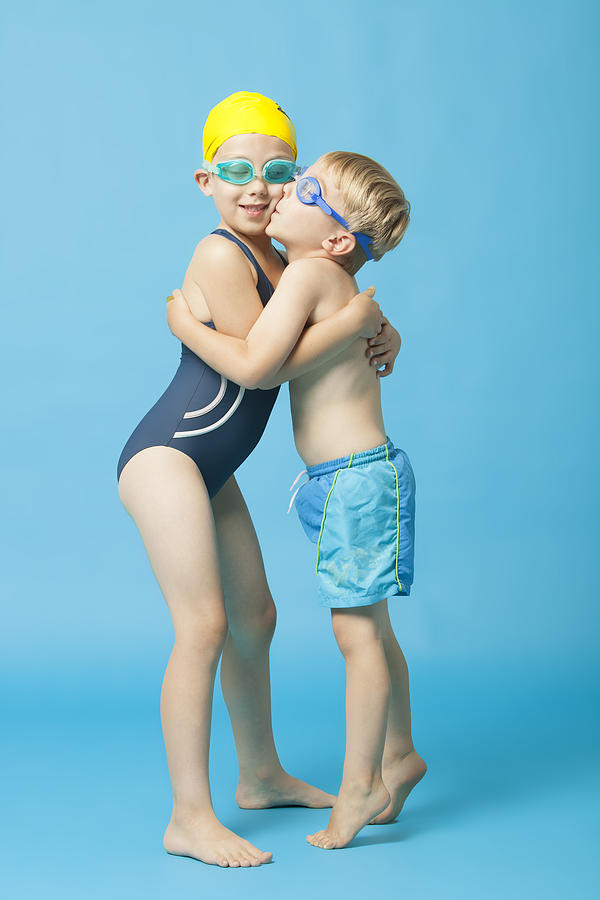 Young siblings in swimwear embracing and kissing over blue background Photograph by Moodboard