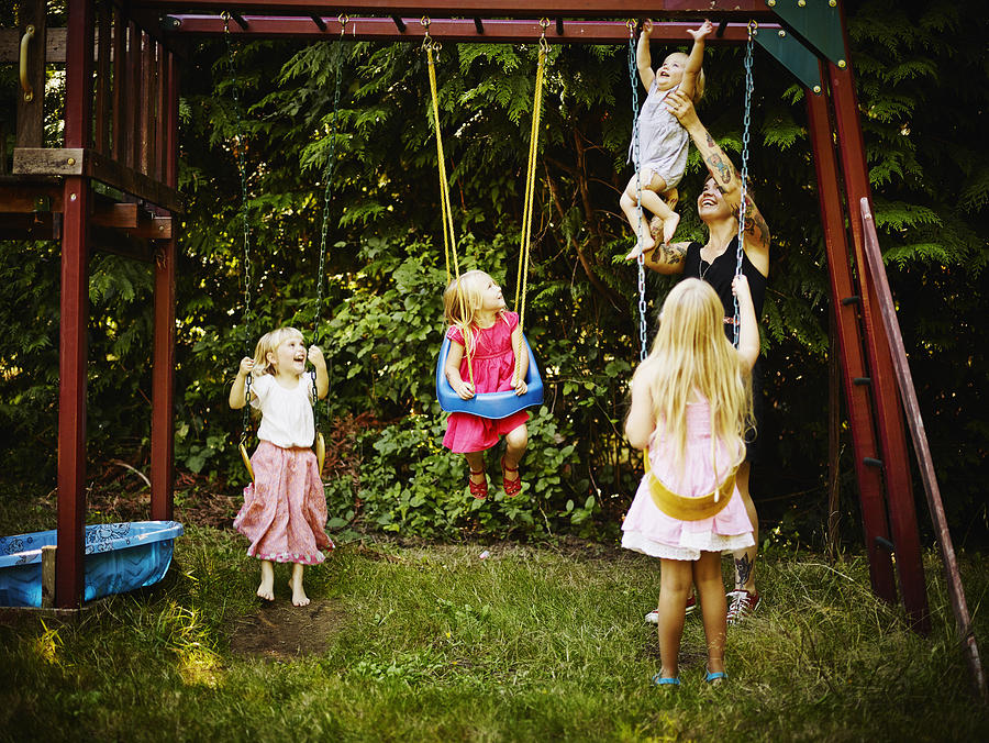 Young sisters on swings and mother holding toddler Photograph by Thomas Barwick