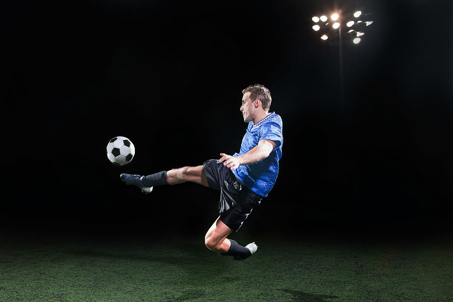 Young soccer player leaping into air to kick ball Photograph by Image Source