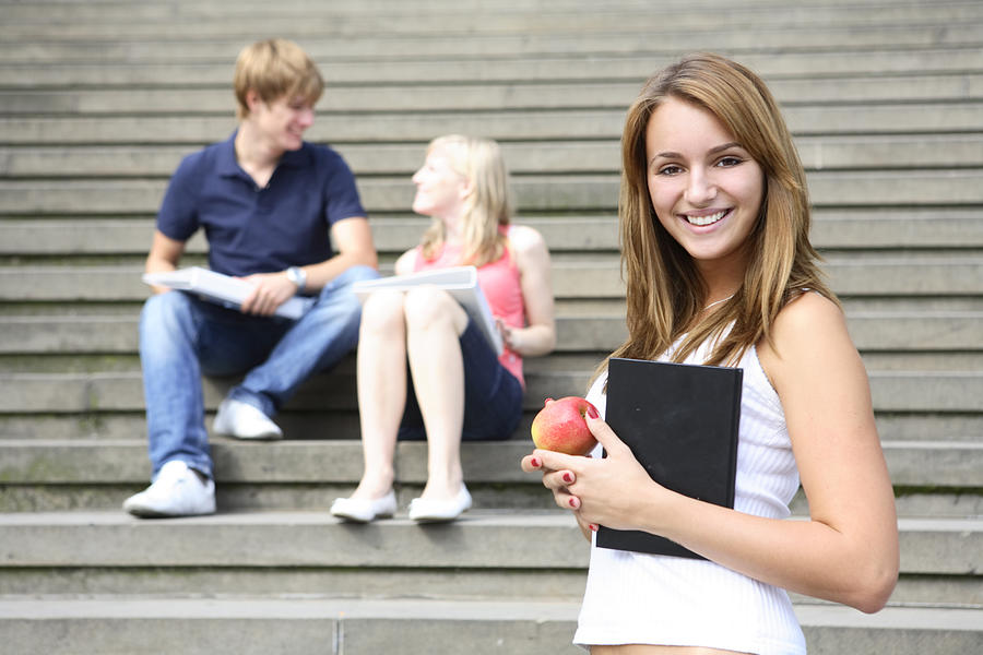 Young student on campus with book and apple. Other students in background Photograph by Luis Alvarez
