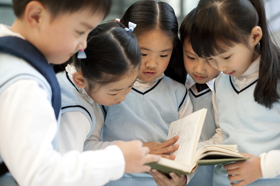 Young students huddle together reading a book Photograph by Lane Oatey/Blue Jean Images