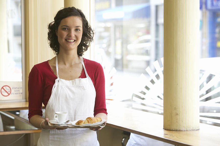 Young waitress holding tray, smiling, portrait Photograph by Rayes