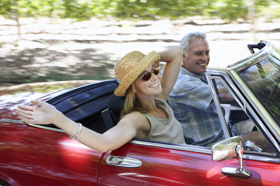 Young Woman and Mature Man Drive in a Convertible Car Photograph by Digital Vision.