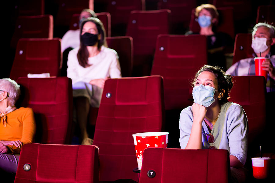 Young woman and the other spectators wearing protective face masks at the cinema Photograph by MixMedia
