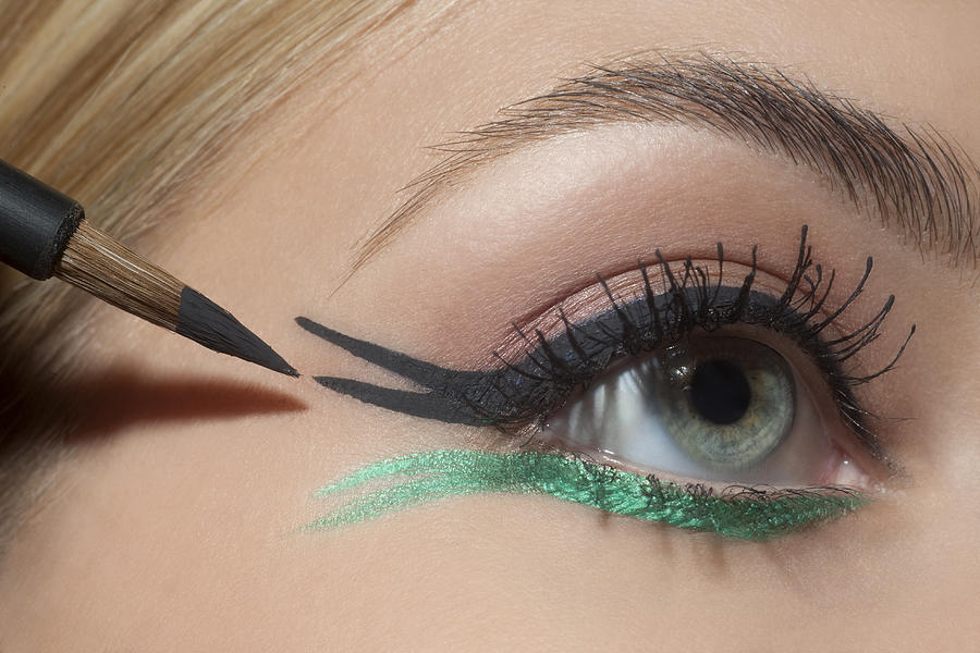 Young woman applying eye make up, close up. Photograph by Andreas Kuehn