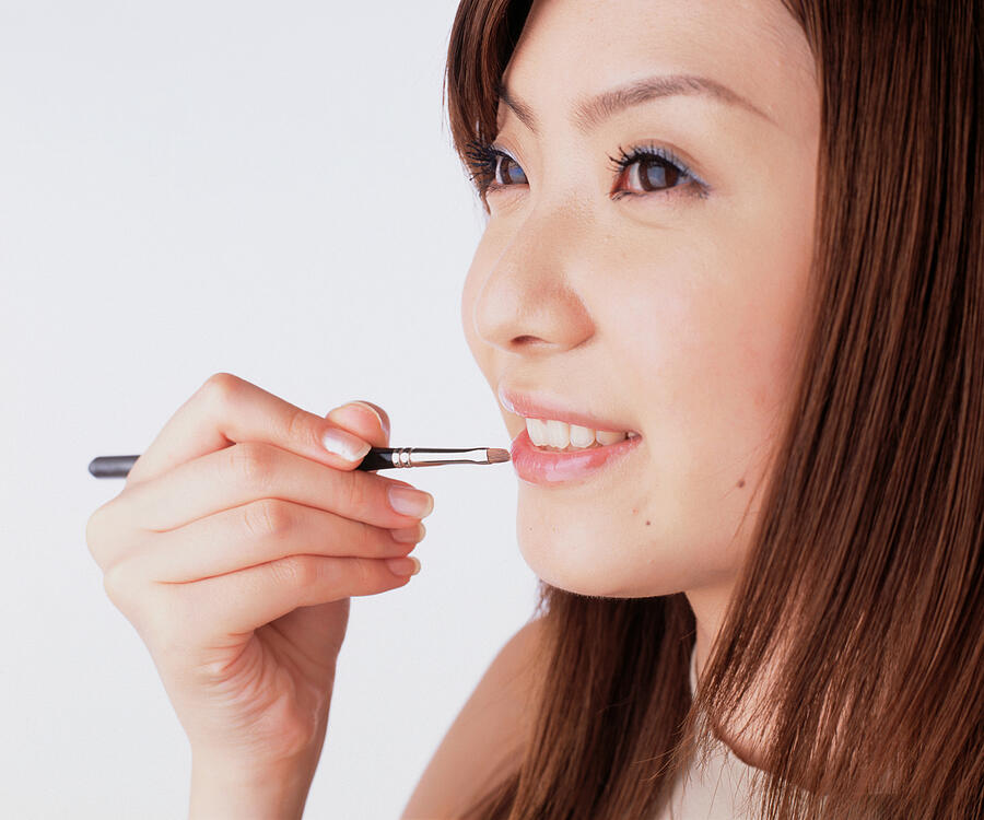 Young woman applying lipstick with a lip brush Photograph by Dex Image