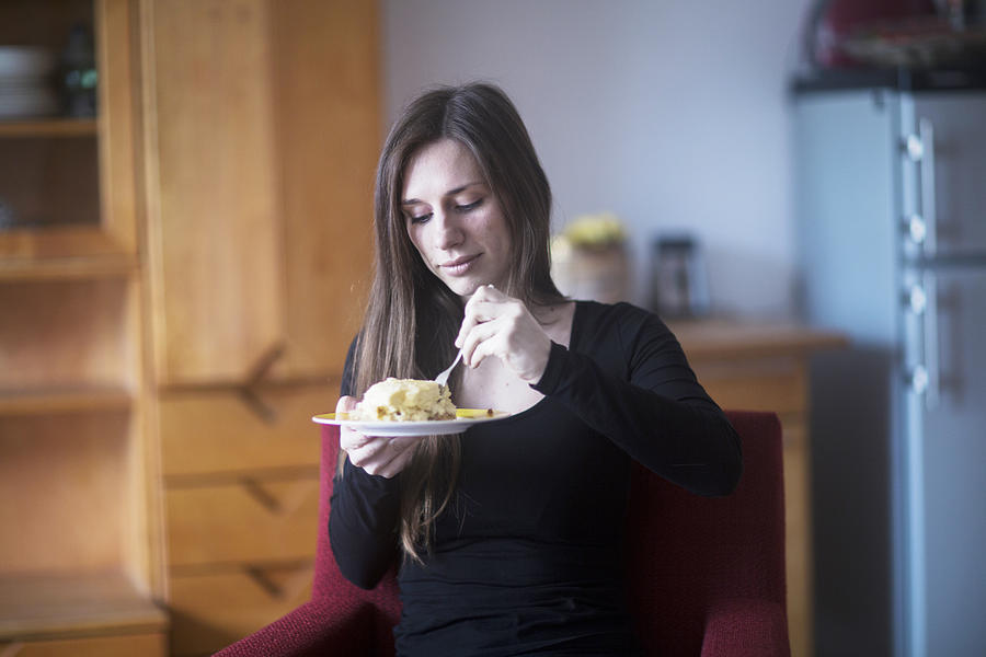 Young woman at home, eating lunch Photograph by Sigrid Gombert