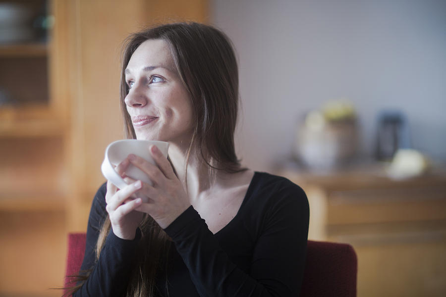Young woman at home, holding hot drink Photograph by Sigrid Gombert