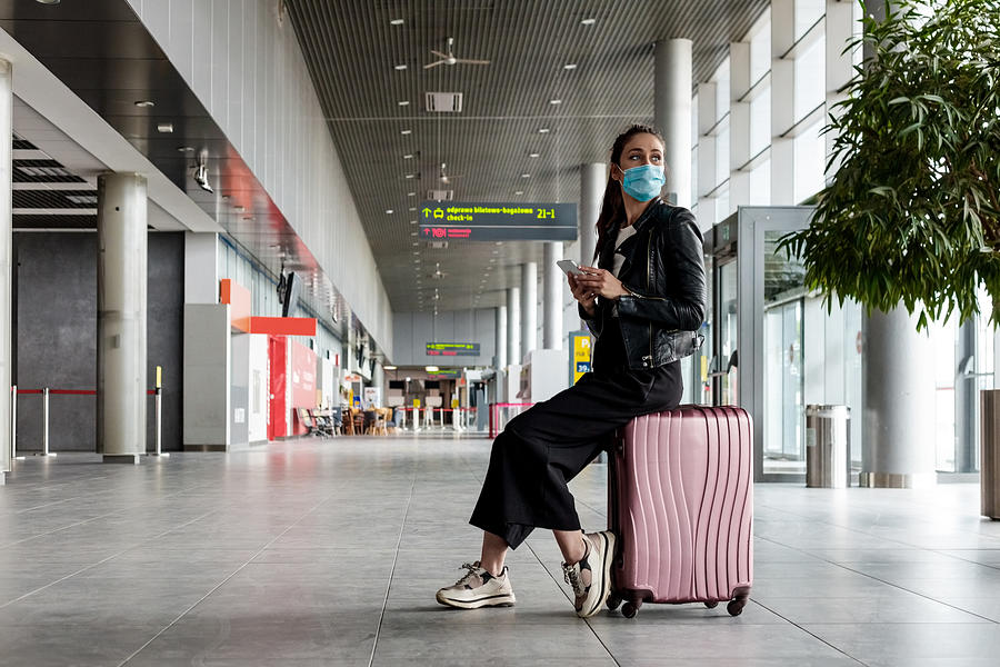 Young woman at the airport with luggage, wearing N95 face masks Photograph by Izusek