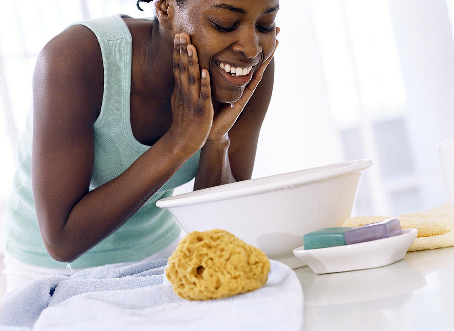 Young woman bent over bowl, washing face, smiling Photograph by Digital Vision