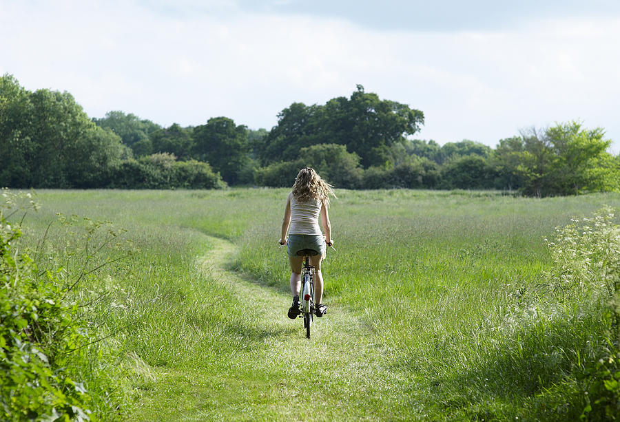 Young woman biking through countryside meadow. Photograph by Dougal Waters