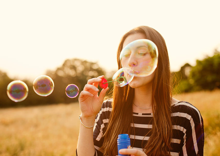 Young woman blowing bubbles in field. Photograph by Tim Robberts