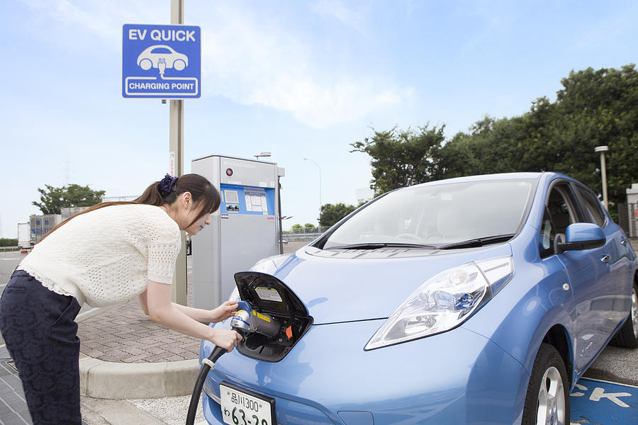 young woman charging Electric Car Photograph by Michael H