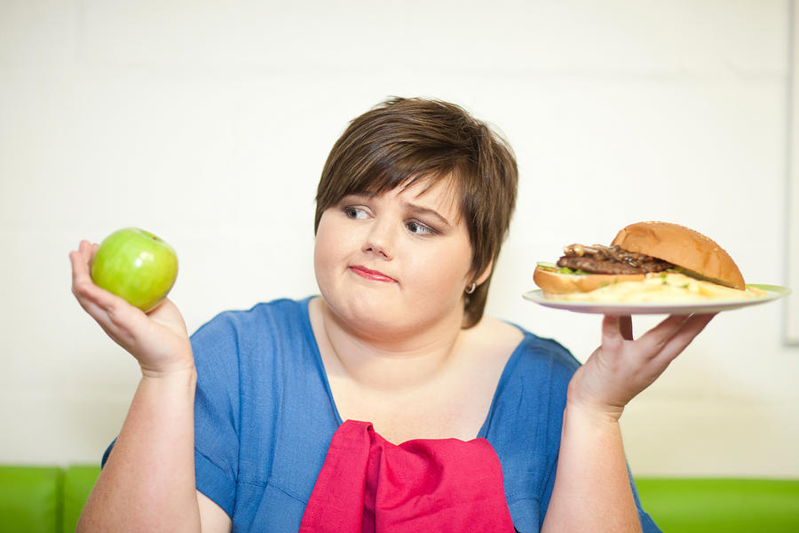 Young woman choosing between an apple and a burger Photograph by Zero Creatives