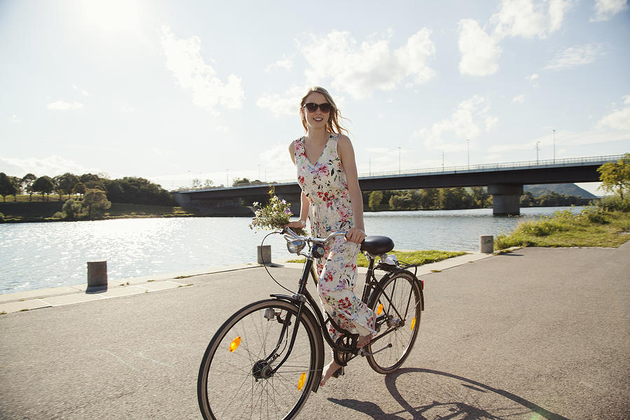 Young woman cycling along riverside, Danube Island, Vienna, Austria Photograph by Manuela