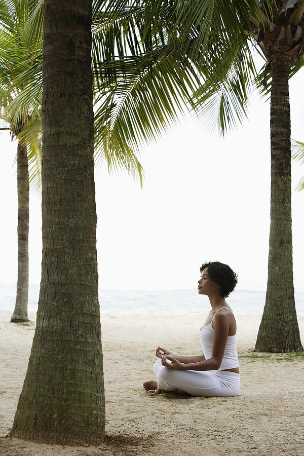 Young woman doing yoga on beach, under coconut trees, meditating. Photograph by Asia Images