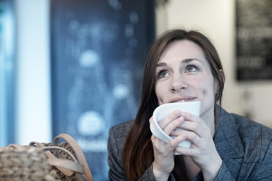Young woman drinking coffee in cafe looking up Photograph by Sigrid Gombert