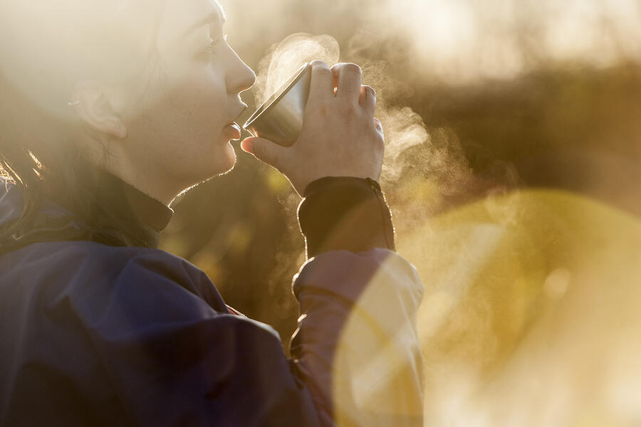 Young woman drinking hot drink in sunlight Photograph by Colin Hawkins