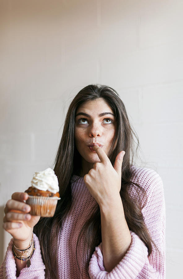Young woman eating a cup cake with whipped cream, licking finger Photograph by Westend61