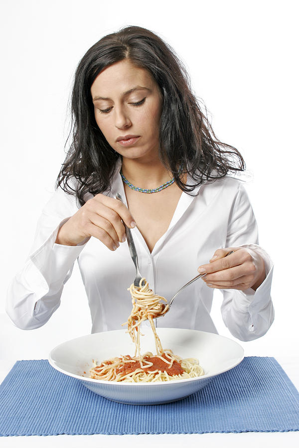 Young woman eating bowl of spaghetti with fork, portrait Photograph by Loop Delay