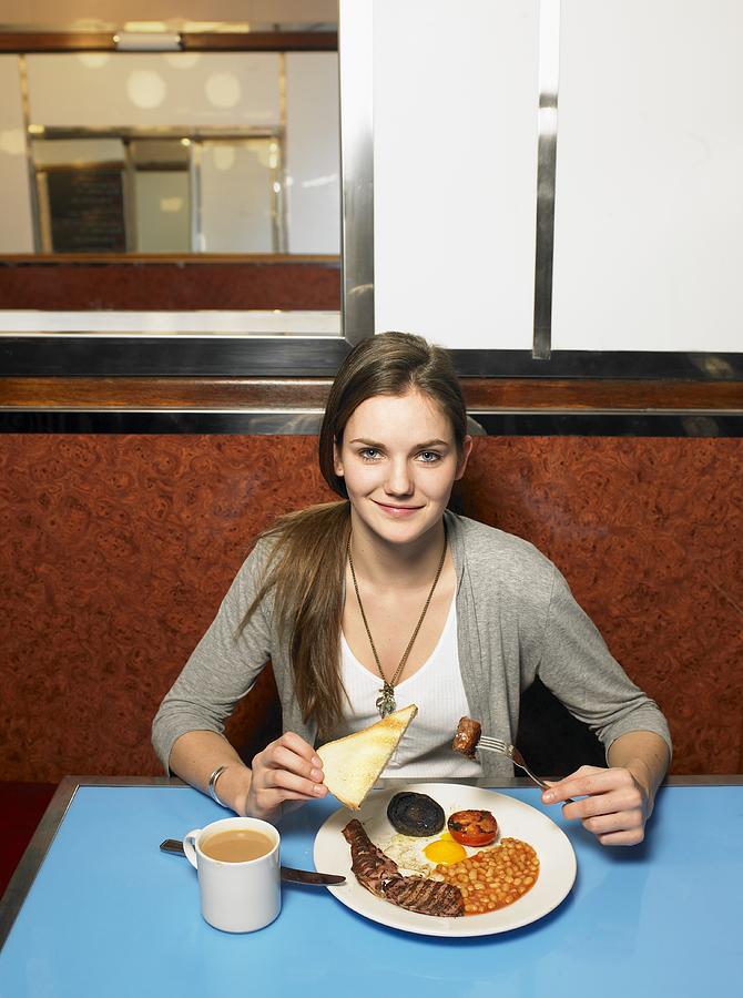Young woman eating fried breakfast in cafe, portrait Photograph by Mel Yates