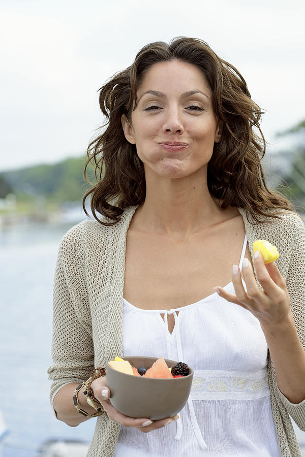 Young woman eating fruit on dock, smiling, portrait, close-up Photograph by Marili Forastieri