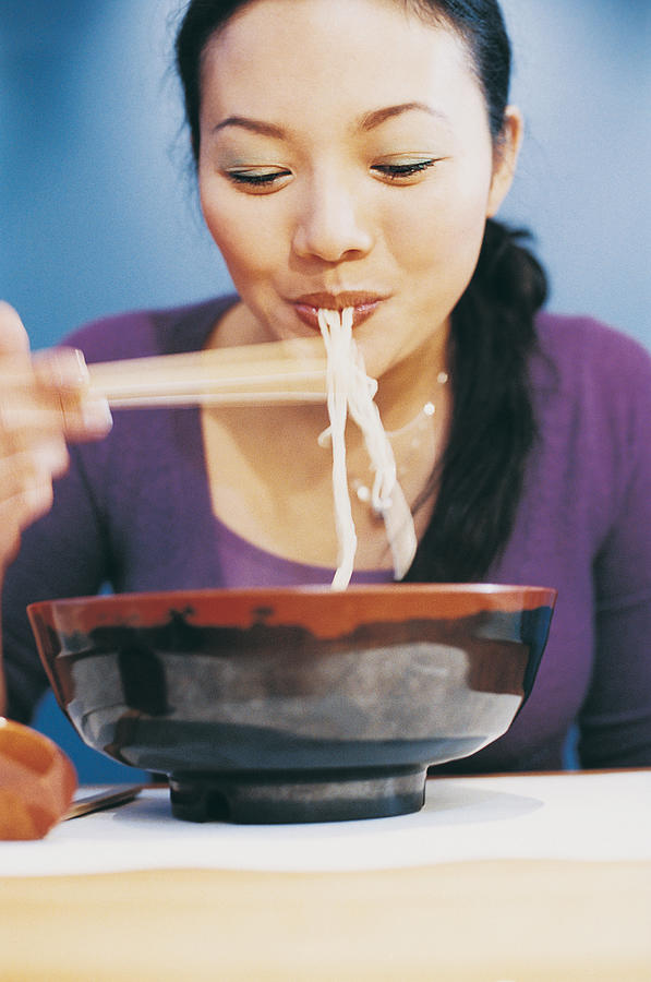 Young Woman Eating Noodles From a Bowl Using Chopsticks Photograph by Digital Vision.
