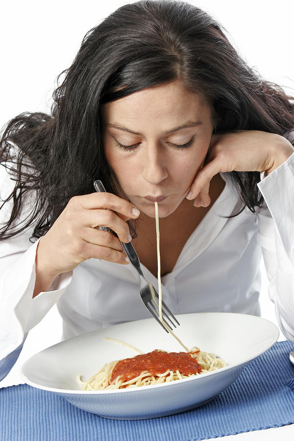 Young woman eating spaghetti with fork, portrait Photograph by Loop Delay