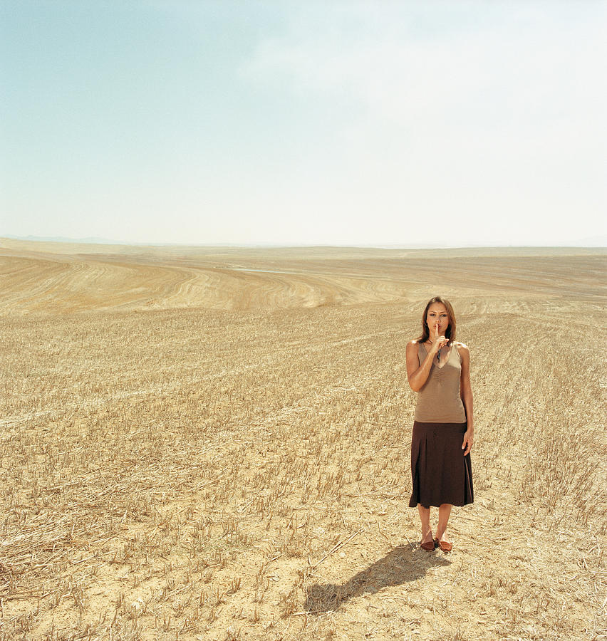 Young woman, finger on lips, in open landscape Photograph by Martin Barraud