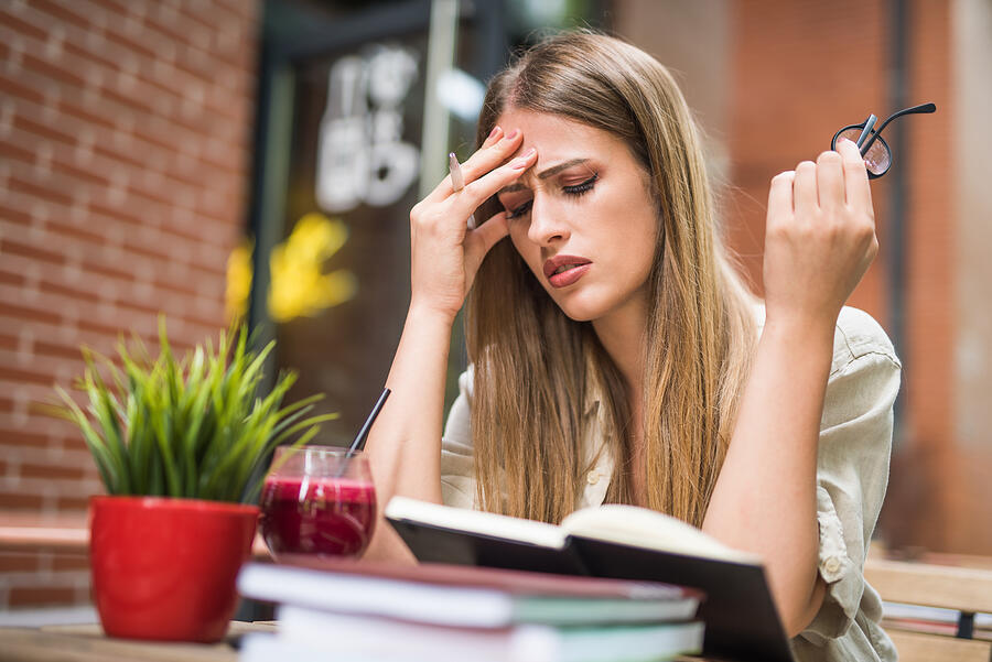 Young woman having a headache from studying. Photograph by DjelicS