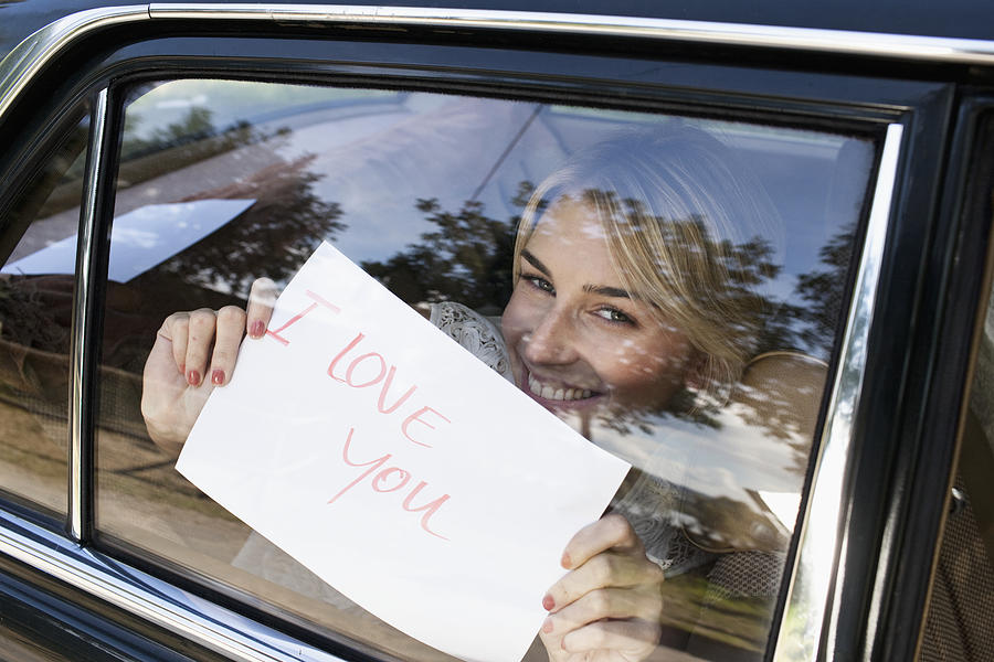 Young woman holding a sign saying I Love You up to a car window Photograph by Oliver Rossi