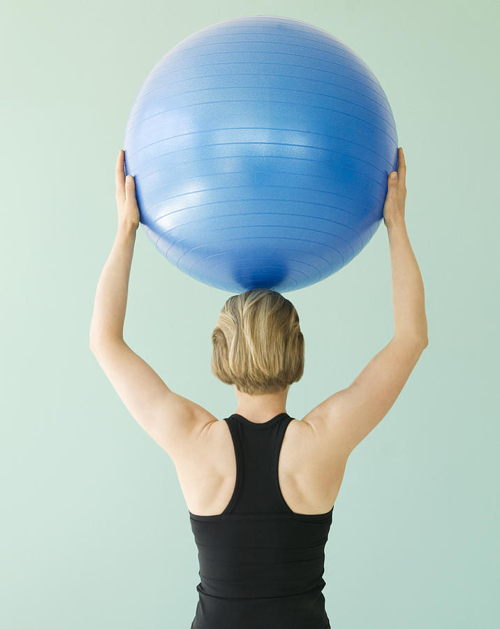 Young woman holding exercise ball above head, rear view Photograph by Caroline Schiff