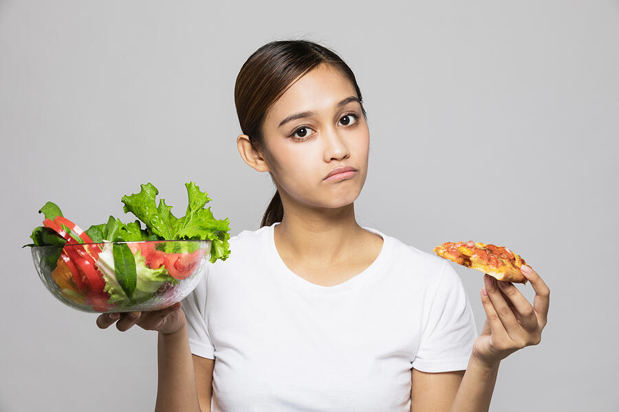 Young woman holding salad bowl and pizza. Photograph by Metamorworks
