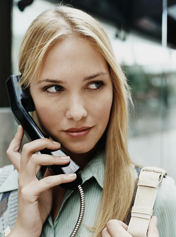 Young Woman Holds the Telephone Receiver of a Payphone Photograph by Digital Vision.