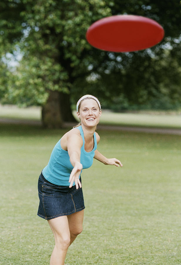 Young Woman in a Park Throwing a Frisbee Photograph by Digital Vision.