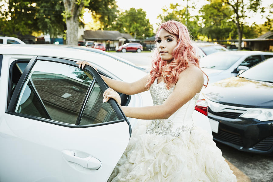 Young woman in gown standing by car before quinceanera Photograph by Thomas Barwick